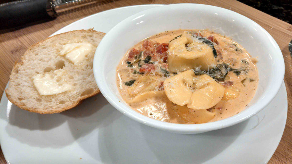 creamy tortelloni soup in a bowl with buttered bread on the side