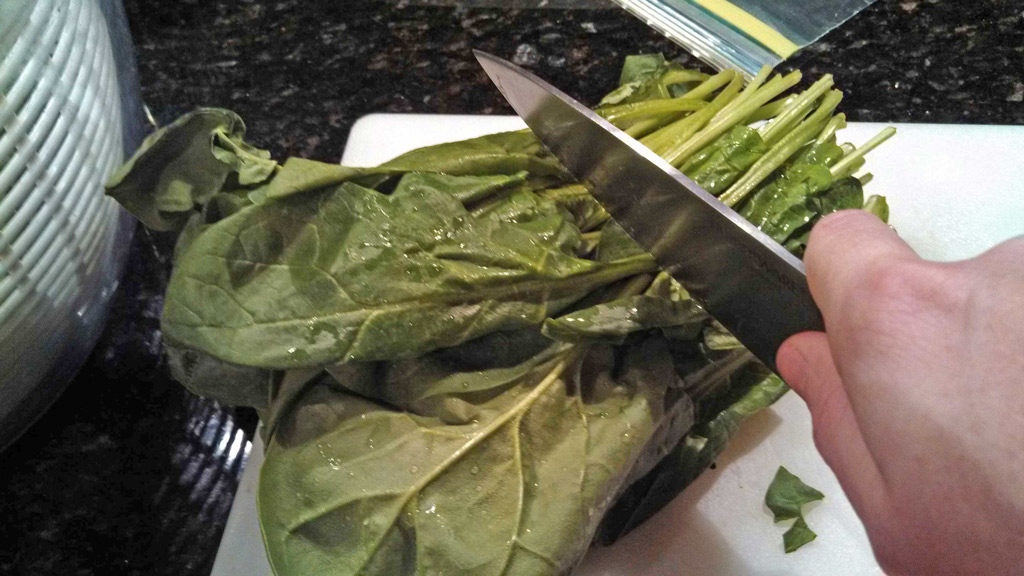 cutting the stems of raw spinach