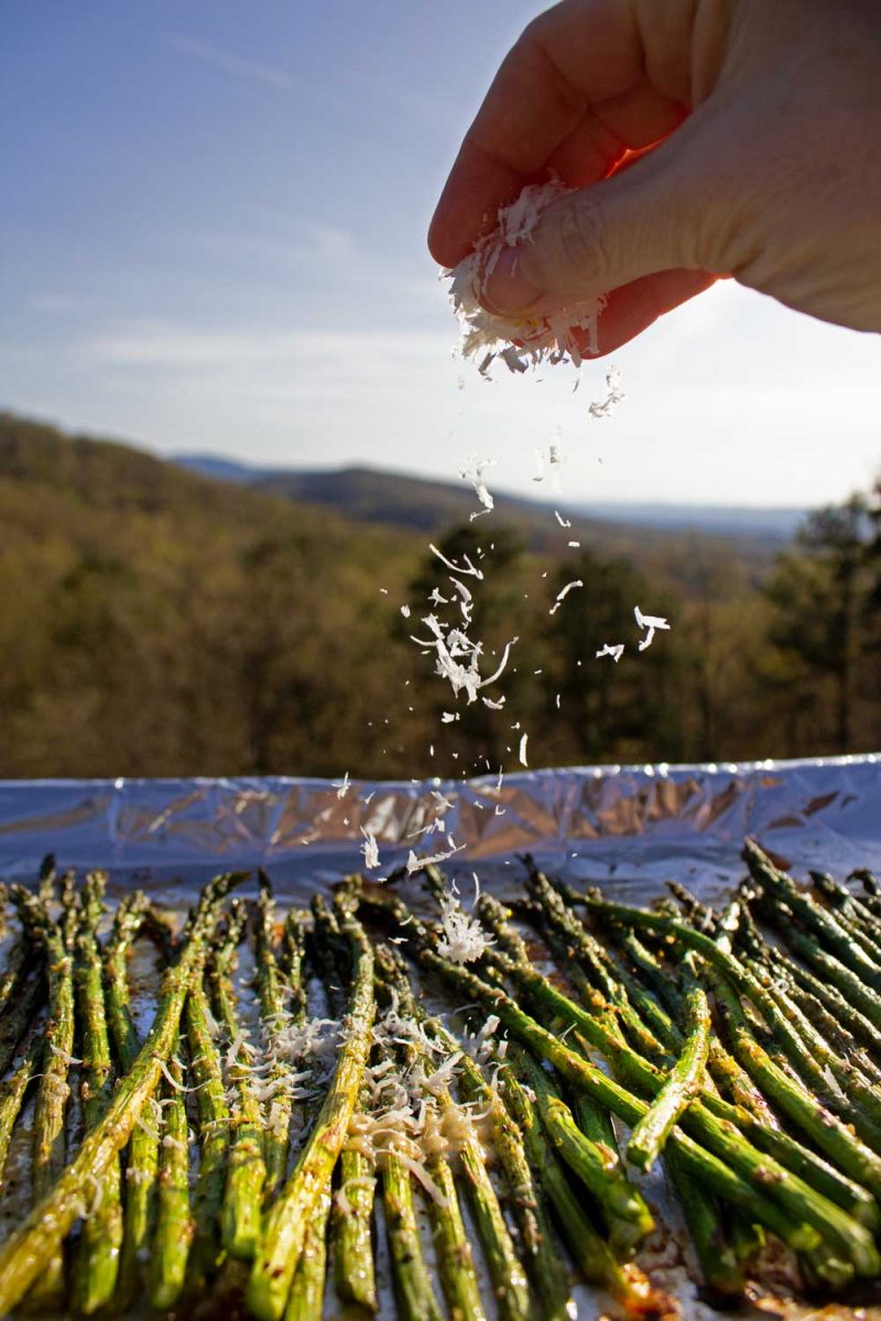 sprinkling freshly grated parmesan over oven-roasted asparagus on a sheet pan