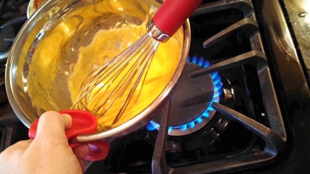whisking Hollandaise sauce in bowl over heat