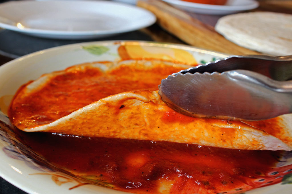 dipping tortilla into enchilada sauce