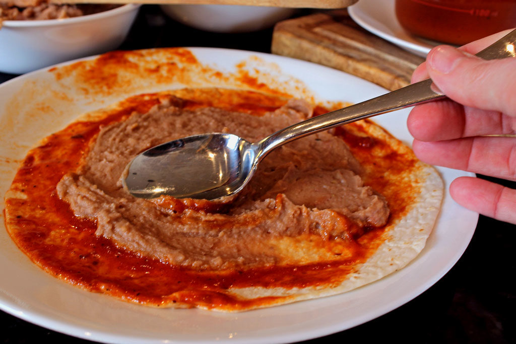 smearing beans onto saucy tortilla