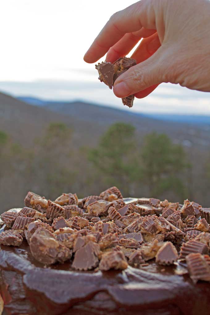 hand tossing peanut butter cups onto Reese's Cheesecake