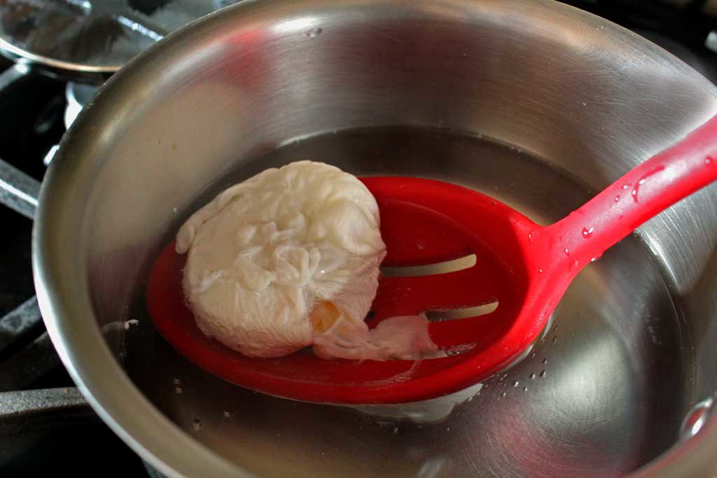 scooping poached egg with slotted spoon