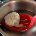 scooping poached egg with slotted spoon