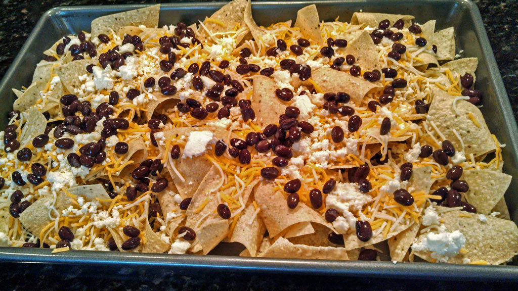 tortilla chips, cheese and black beans on a sheet pan