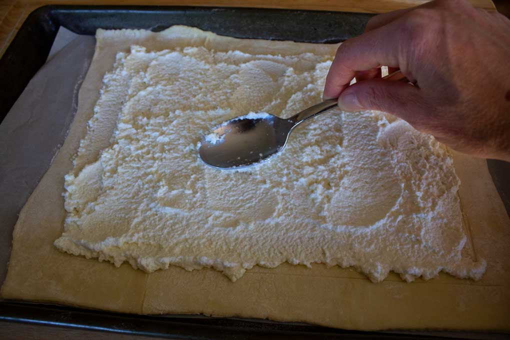smearing ricotta onto puff pastry with spoon