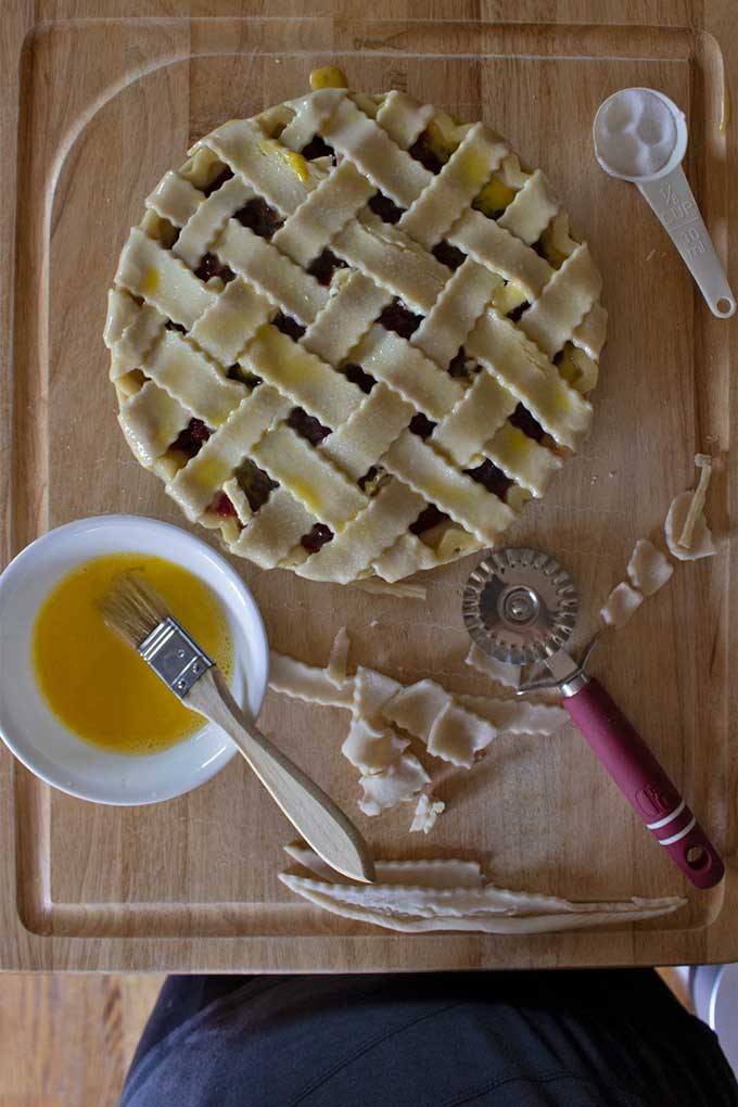 prepared homemade cherry pie on board with bowl of egg wash and extra pastry dough
