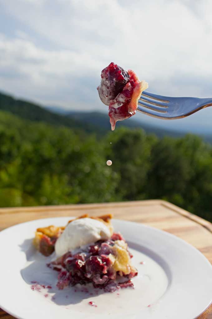 bite of homemade cherry pie on fork with dripping ice cream and mountain view
