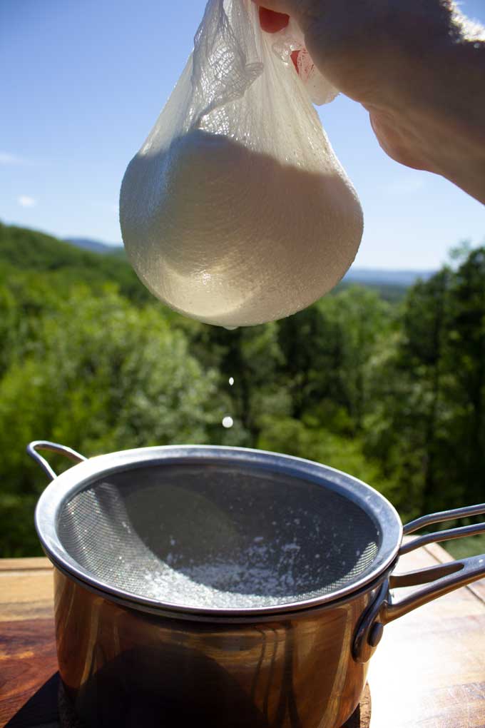 homemade ricotta cheese dripping through cheesecloth with mountain view