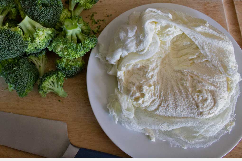 ricotta cheese in cheesecloth on cutting board with broccoli