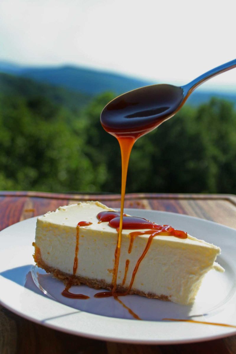 drizzling caramel sauce on top of cheesecake slice with mountain view