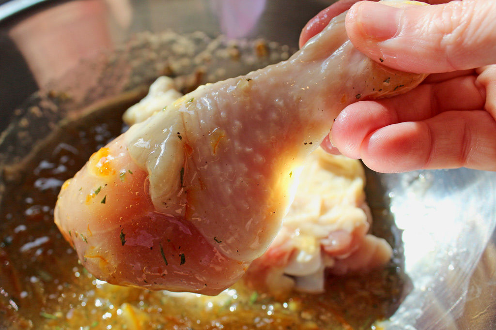 hand dipping chicken leg into sauce