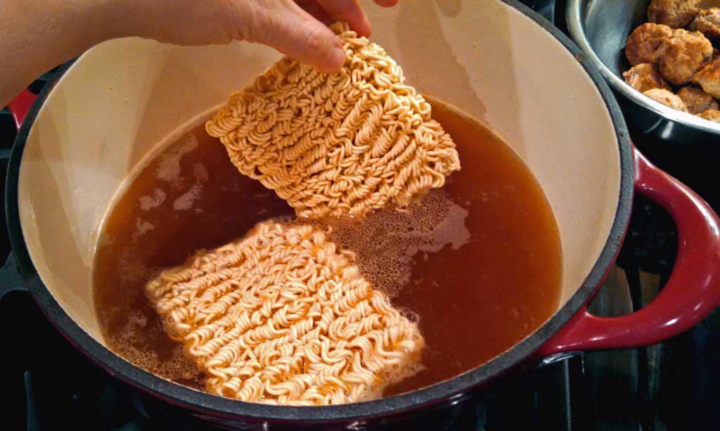 adding noodles to the pot of broth