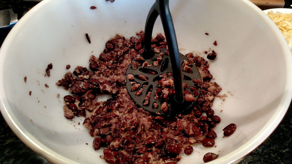 smashing black beans with potato masher