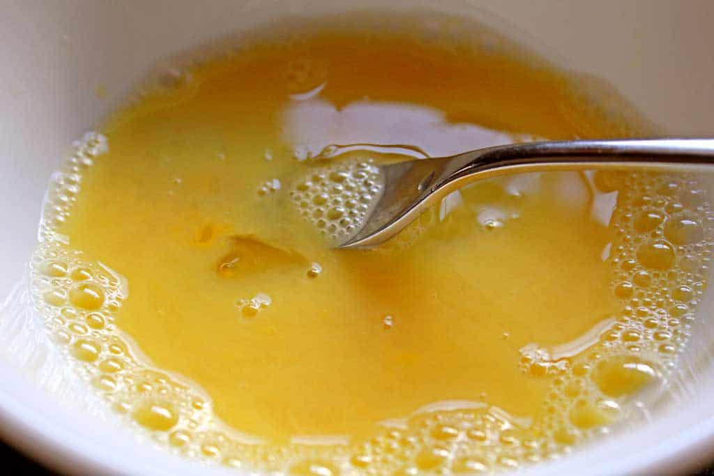 egg and water in bowl with fork to whisk