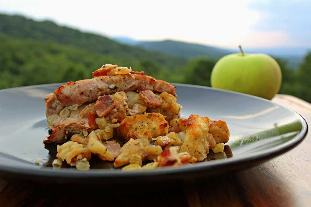 pork chops with apple-bacon stuffing on plate with an apple and mountain view