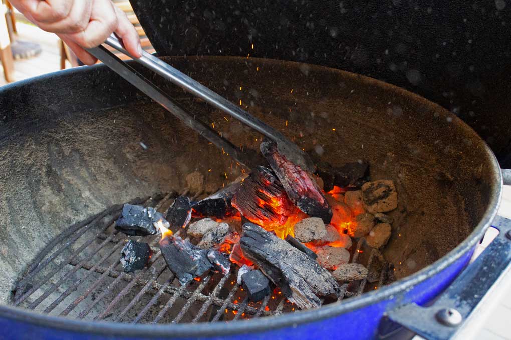 utility tongs tending coals inside grill