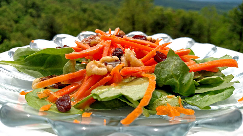 This healthy carrot salad with homemade dressing is served on top of a bed of spinach with juicy raisins, and candied walnuts. It was delicious! | TheMountainKitchen.com