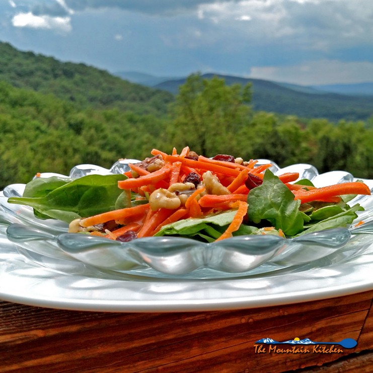 This healthy carrot salad with homemade dressing is served on top of a bed of spinach with juicy raisins, and candied walnuts. It was delicious! | TheMountainKitchen.com