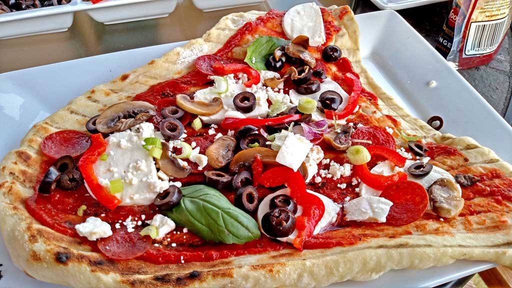 The grilled pizza with all the toppings ready to go back on the grill.