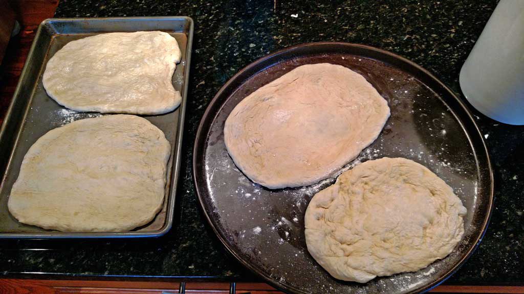 Pizza dough laid out on baking sheets ready for the grill.