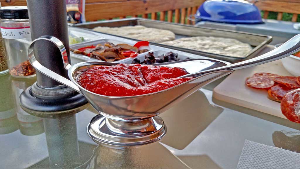 A silver gravy boat full of pizza sauce, ready for the grilled pizza.