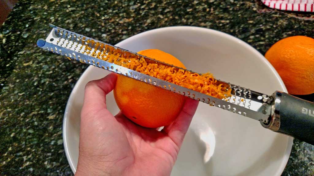 zesting orange with microplane over bowl