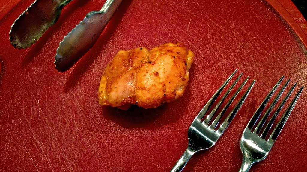 chicken thigh on cutting board with tongs and two forks