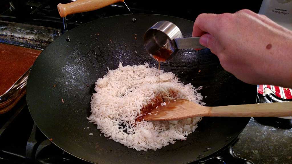 pouring reserved juice into rice inside wok