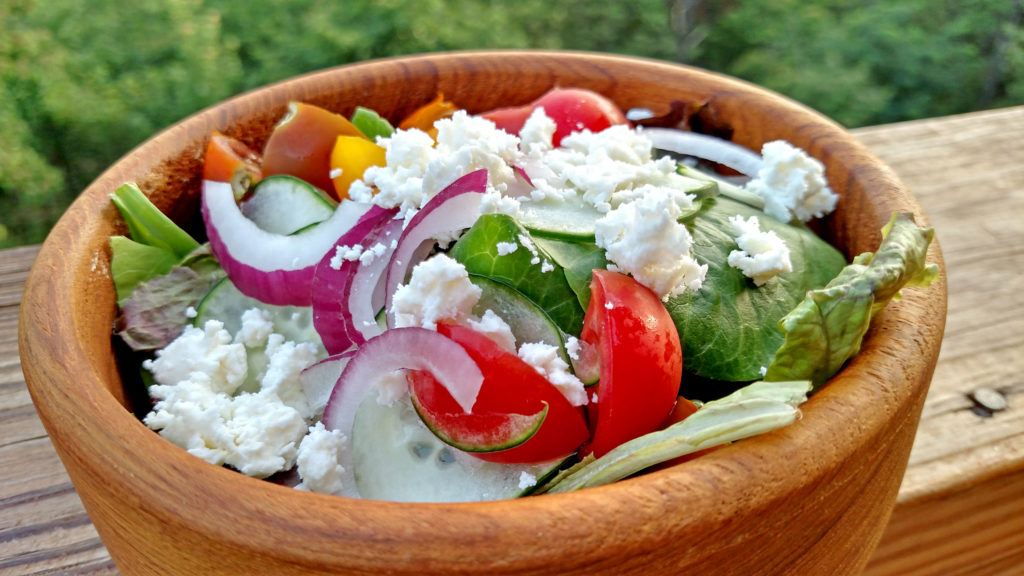 Greek salad made of tomatoes, cucumber, sliced red onion, feta cheese and black olives on a bed of fresh salad greens and drizzled with Greek dressing. | TheMountainKitchen.com