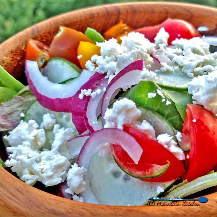 Greek salad made of tomatoes, cucumber, sliced red onion, feta cheese and black olives on a bed of fresh salad greens and drizzled with Greek dressing. | TheMountainKitchen.com