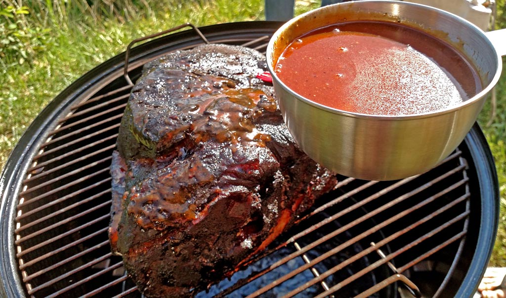 putting sauce on the smoking pork butt