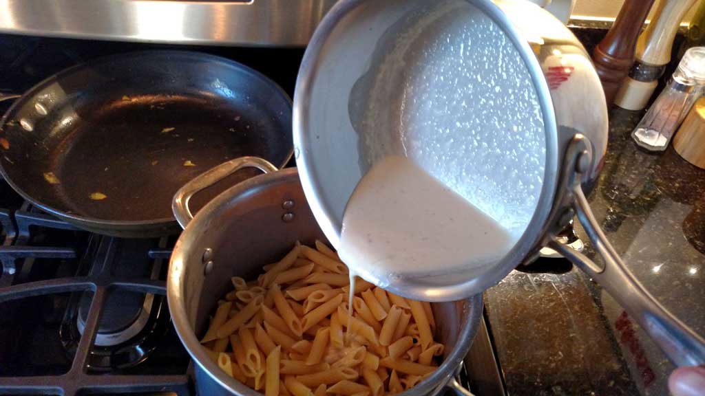 pouring the alfredo sauce into pasta