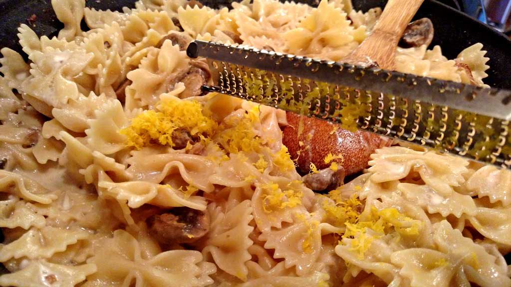 using microplane to zest lemon peel into pasta