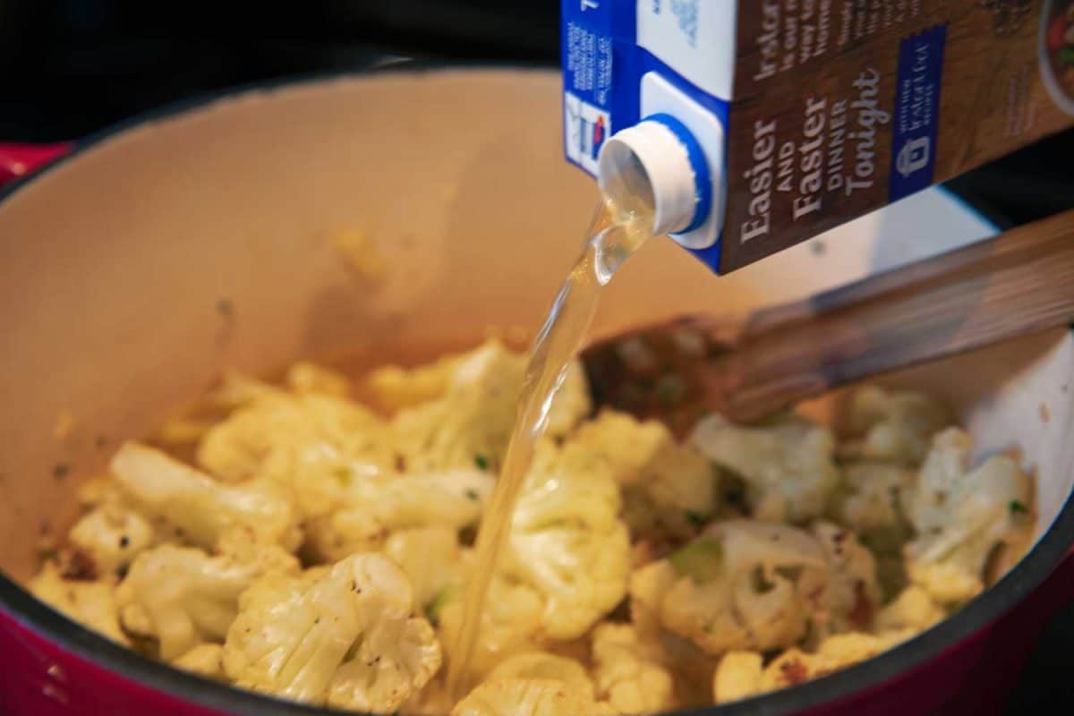 pouring broth into pot of roasted cauliflower soup