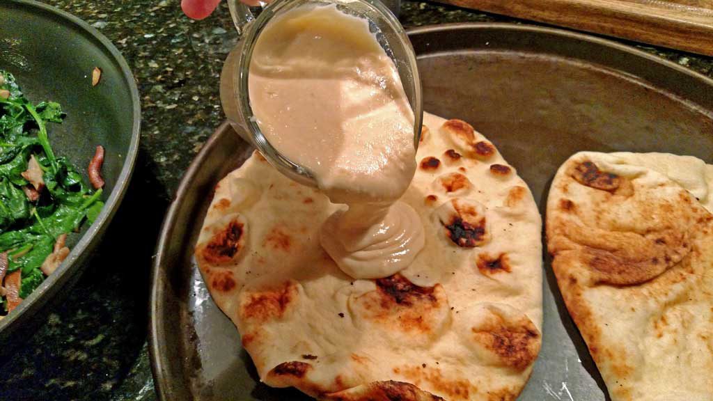 pouring the Alfredo sauce onto the flatbread