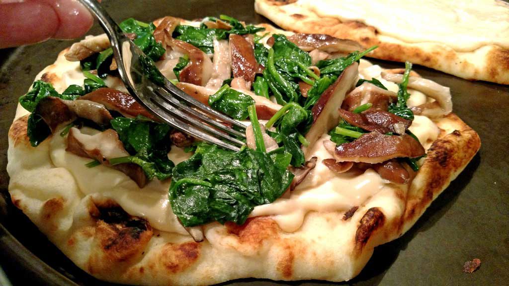 topping the Alfredo covered flatbread with spinach and mushrooms
