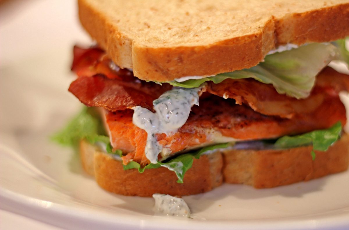 salmon blt sandwich with yogurt dill sauce dripping on plate