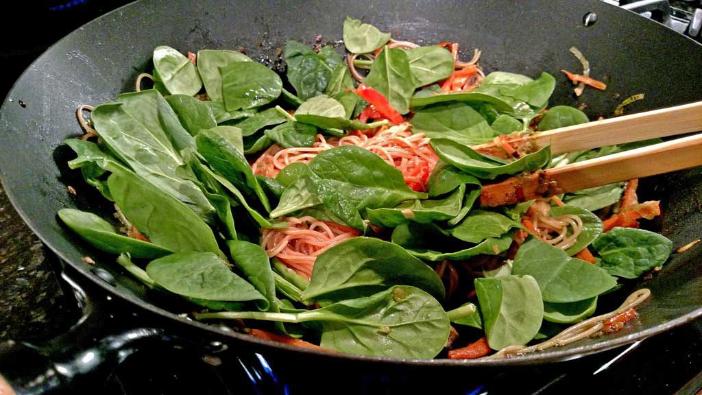 spinach cooking in wok with pasta and vegetables