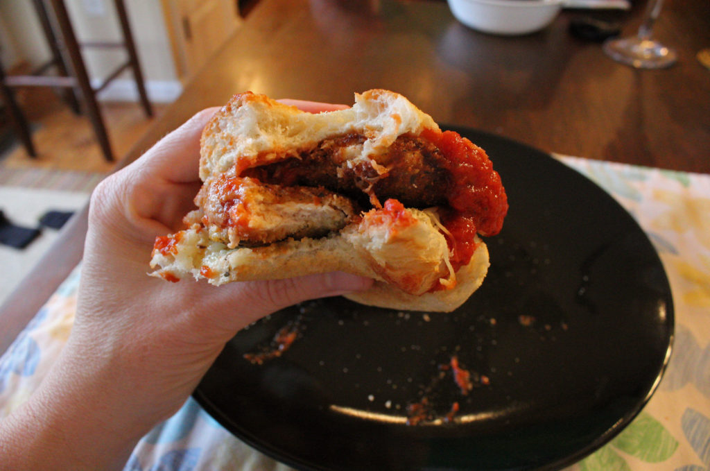 hand with bite taken out of chicken parmesan sub sandwiches
