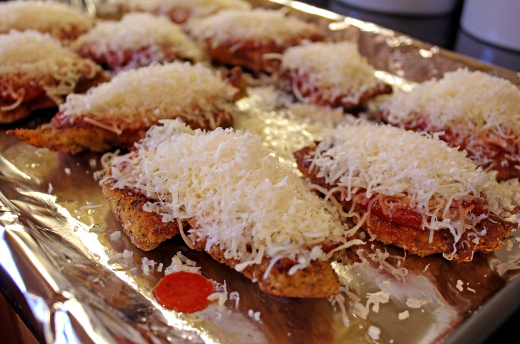 chicken on baking sheet covered in sauce and cheese
