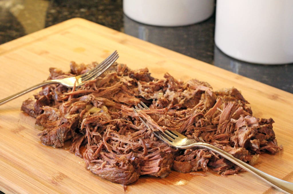 shredded beef on cutting board with forks