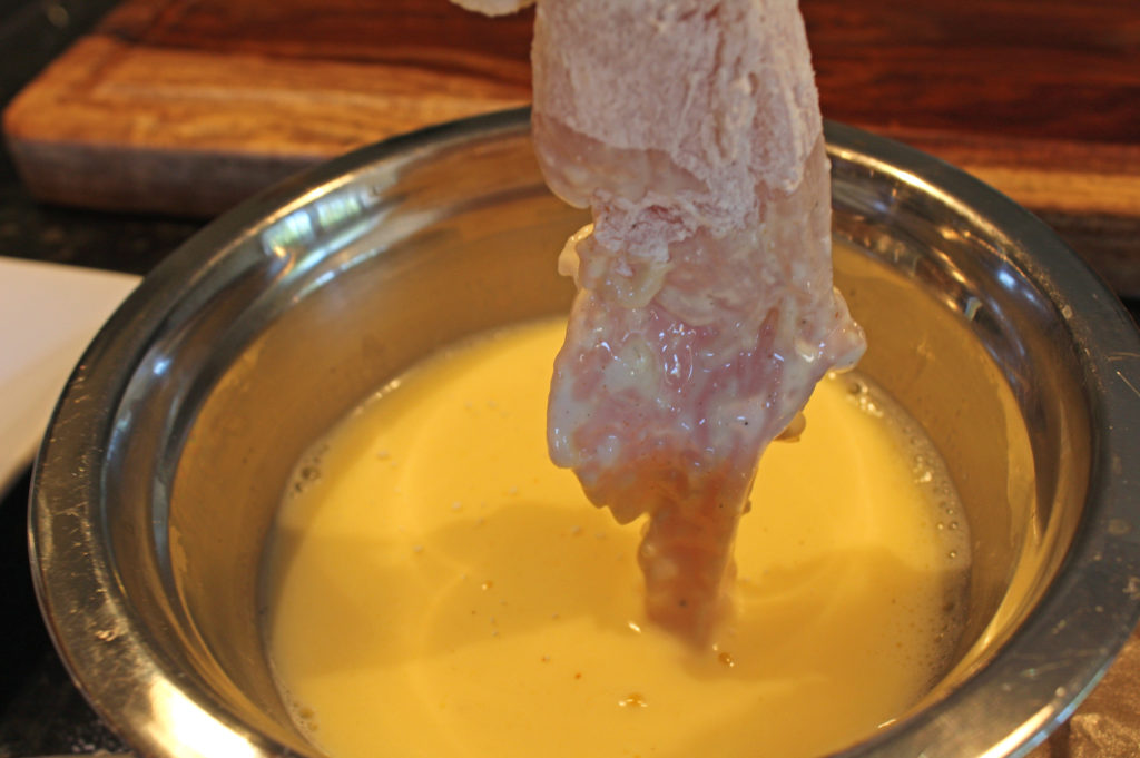 dipping flour covered chicken into egg mixture