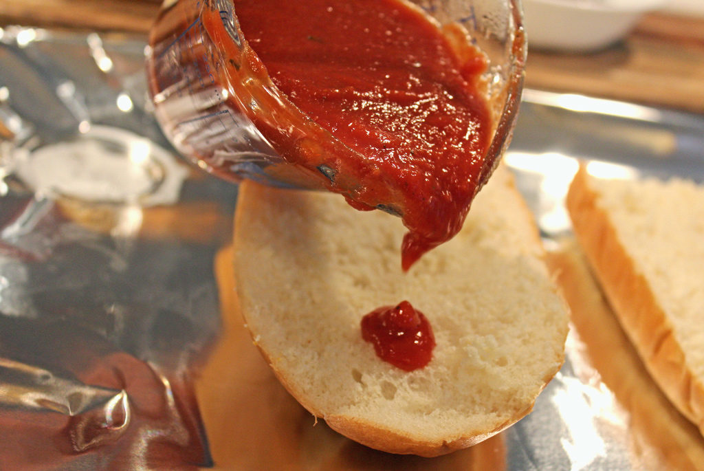 pouring pizza sauce onto French bread
