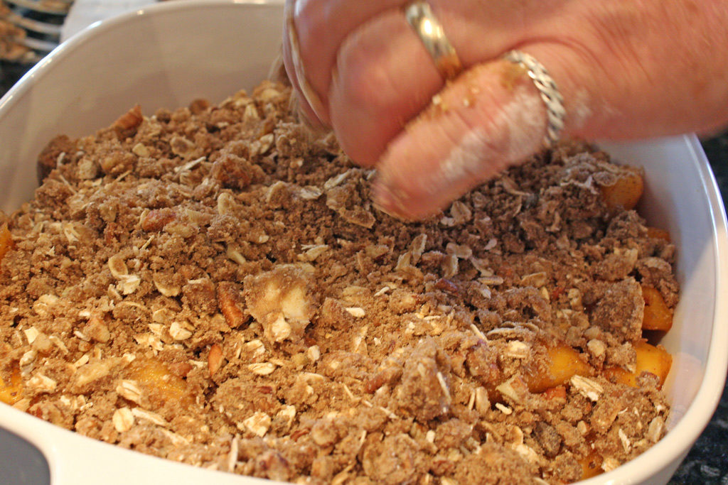 David's hand sprinkling the topping on the peach crisp