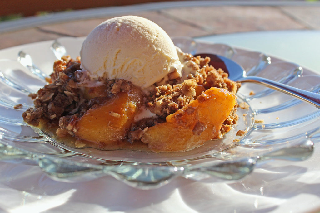 cinnamon peach crisp on plate with ice cream on top