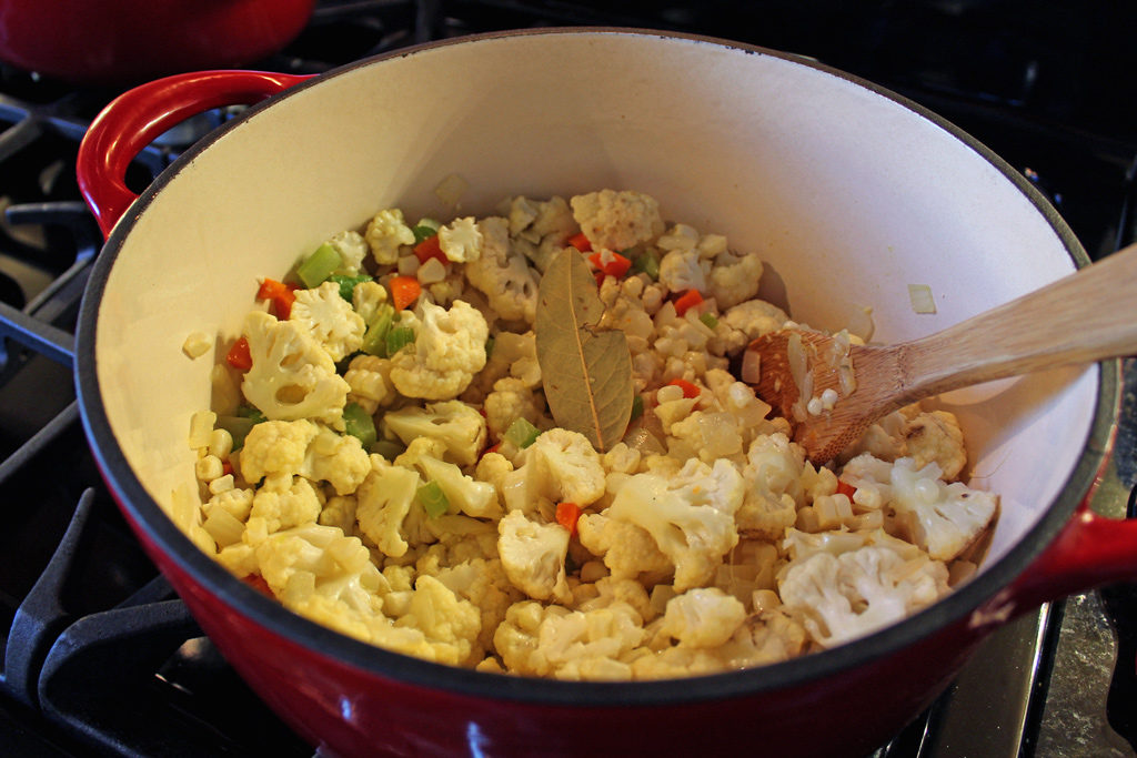 The cauliflower and bay leaf added to the vegetables in the pot.