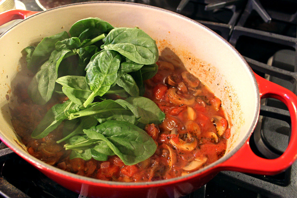fresh raw spinach in pot of sauce
