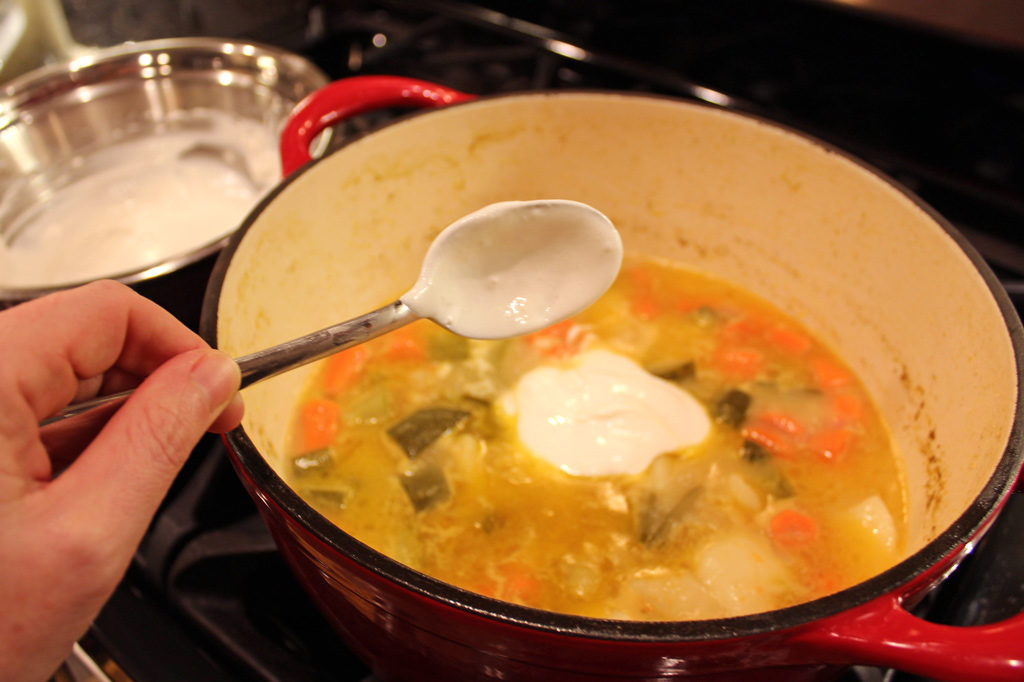 spoon with sour cream going into pot of vegetables